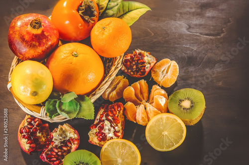 Fototapeta Naklejka Na Ścianę i Meble -  citrus fruits in a wooden basket. orange, pomegranate, mandarin, persimmon, kiwi. on a dark wooden board.