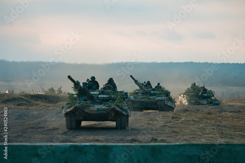 Tanks in row masked at pine tree branches in polygon