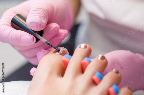 Nail Care And pedicure concept. Closeup Manicurist hands in pink gloves is Painting gold Nail Polish On Client s toes. Woman In Beauty Salon.