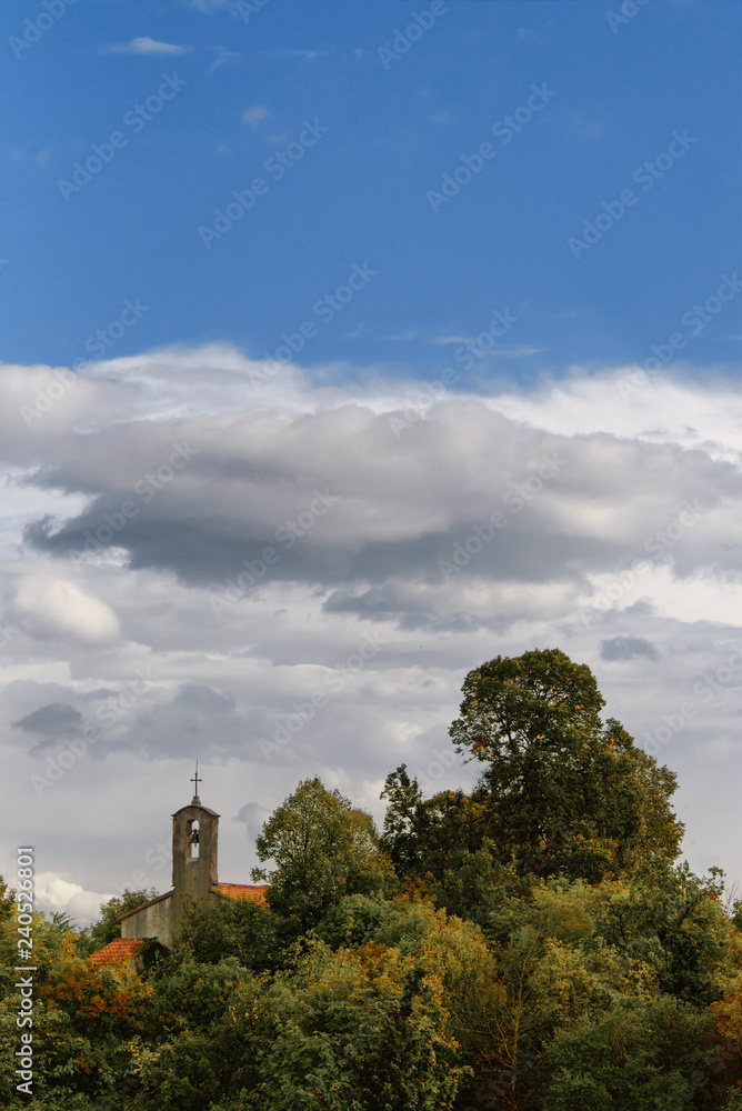 Beautiful vertical landscape from Croatia with the little church and the green trees in foreground, and with clouds and blue sky in the background