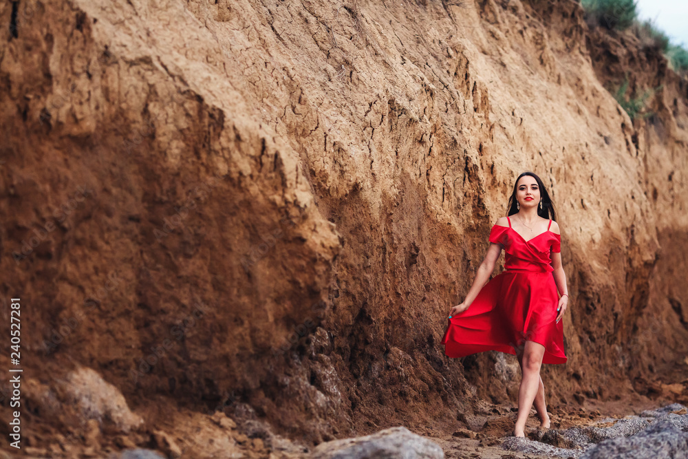 beautiful woman in red dress posing on clay cliff background.