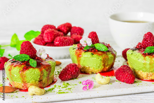 Fototapeta Naklejka Na Ścianę i Meble -  matcha green tea vegan raw cheesecakes with raspberries, mint, nuts and flowers. healthy delicious food
