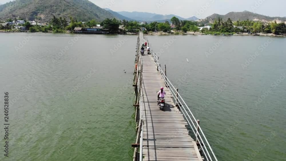 A flying camera follows a motorcyclist riding an old small wooden bridge across a river in an Asian village near Nha Trang Vietnam from a drone. A flying camera follows a motorcyclist riding an old small wooden bridge across a river in an Asian village near Nha Trang Vietnam from a drone.