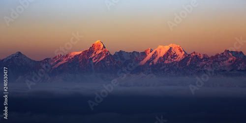 Mountain Range Sunrise, mountains glowing in the sunshine at dawn. Snow covered mountain peaks in the distance, panoramic view. Purple, Orange atmosphere. Sichuan Province China. Rugged wilderness © Cedar