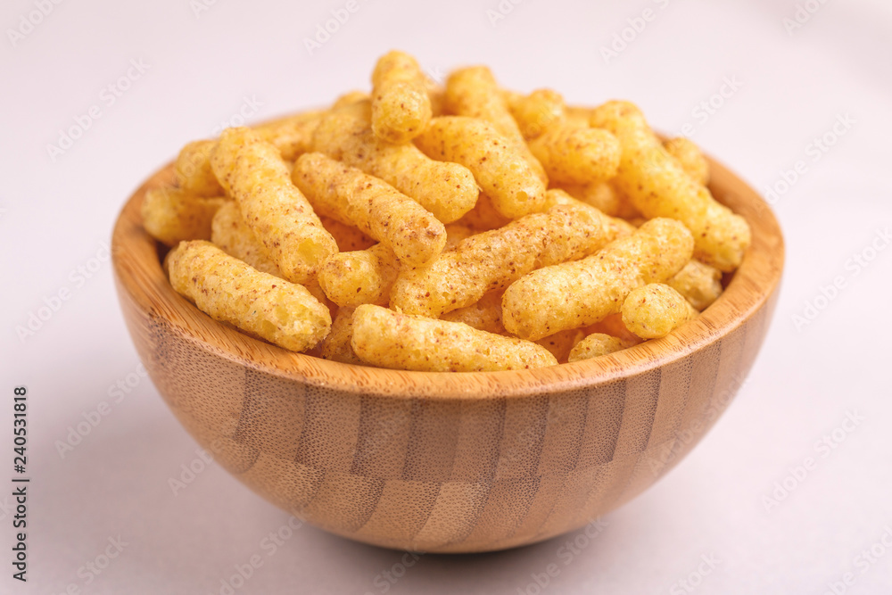 Crispy corn sticks in wooden bowl on light background Crispy corn sticks in wooden bowl on light background