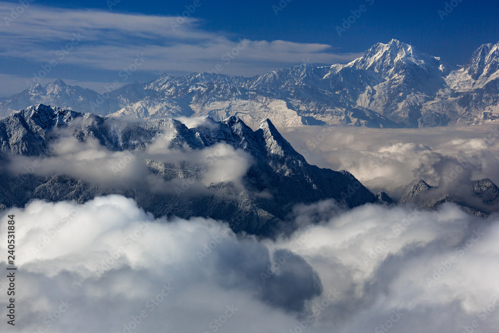 Snow covered Himalayan Mountains above the clouds, mountain peaks above the sea of clouds. mountaineering adventure and trekking concept, winter snowstorm, white puffy clouds floating between peaks