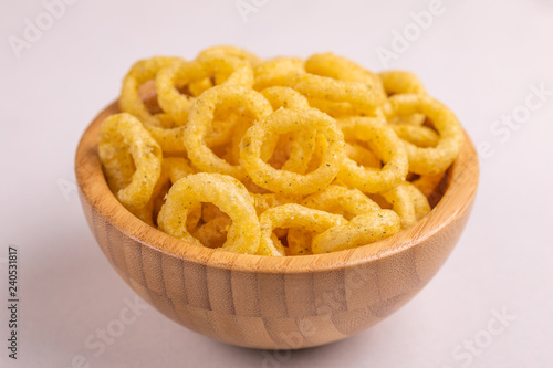 Puff corn rings in wooden bowl on light background