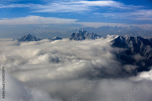 Snow covered Himalayan Mountains above the clouds, mountain peaks above the sea of clouds. mountaineering adventure and trekking concept, winter snowstorm, white puffy clouds floating between peaks © Cedar