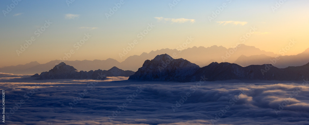 Mountain Range Sunset, mountains glowing in the sunshine at sundown. Snow covered mountain peaks in the distance, panoramic view. Purple, Orange atmosphere. Sichuan Province China. Rugged wilderness