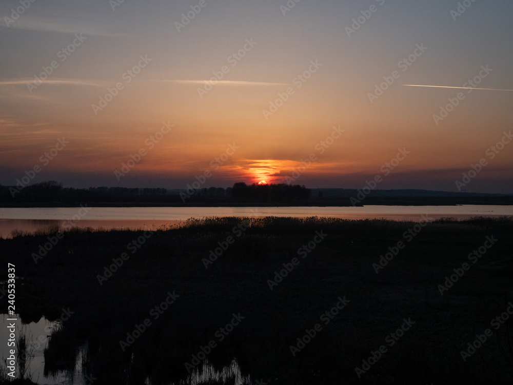 evening rural sunset over small river and forest. low key image. sun is almost disappeared under horizon line