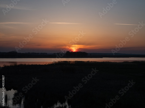 evening rural sunset over small river and forest. low key image. sun is almost disappeared under horizon line