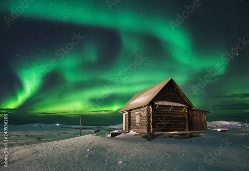 Landscape with northern lights over a wooden house on the coast of the Barents Sea on the Kola Peninsula at night at high ISO sensitivity