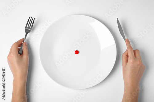 Woman holding cutlery near plate with weight loss pill on white background, top view
