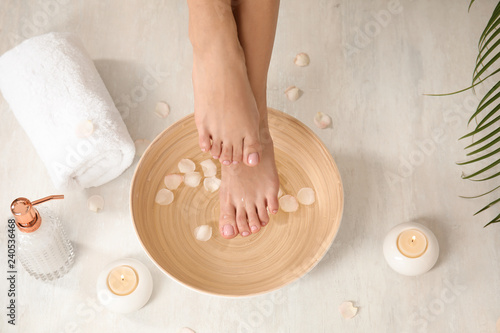 Woman holding her feet over bowl with water and rose petals on floor, closeup. Spa treatment