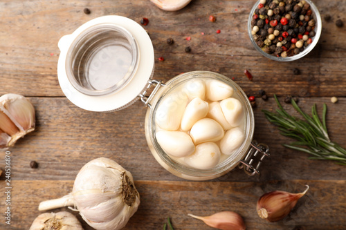 Preserved garlic in glass jar on wooden table, flat lay