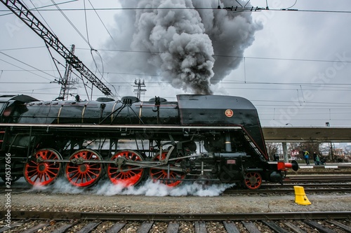 Prague, Czech Republic / Europe - December 15 2018: Old black steam engine, red wheels, made in 1948 running on railway track at Smichov train station, belching out thick grey steam, snowing