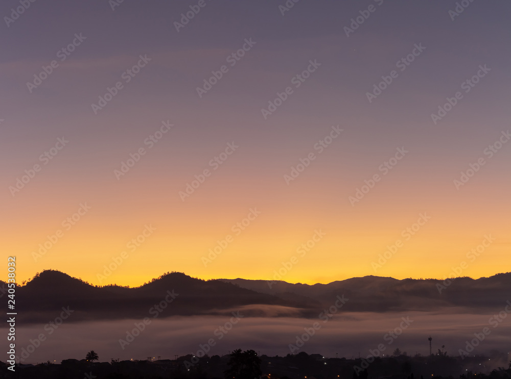 A village surrounded by mountains with foggy morning time and orange sky, beautiful landscape