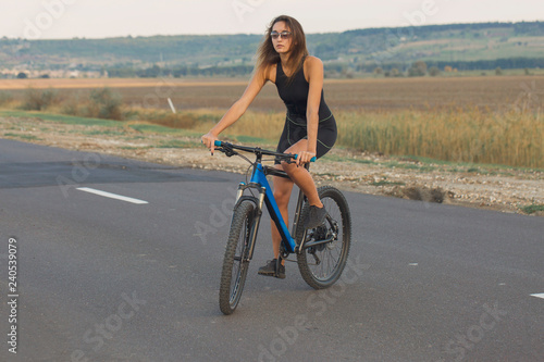 A girl riding a mountain bike on an asphalt road, beautiful portrait of a cyclist at sunset 