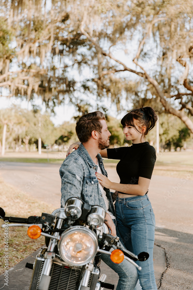 Portrait of Attractive Good Looking Young Modern Trendy Fashionable Guy Girl Couple Riding on Green Motorcycle Cruiser Old School Classic Vintage Bike Smiling Casual Cool Relaxed Dating Hugging Love