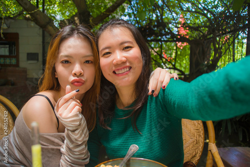 young happy and cute Asian Chinese girlfriends taking selfie portrait picture with mobile phone camera for using on internet social media while having healthy brunch at cafe photo