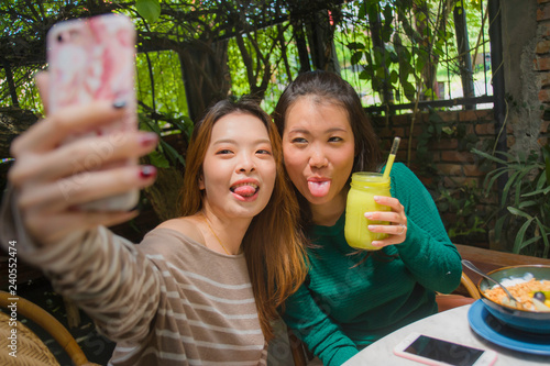 young happy and cute Asian Chinese girlfriends taking selfie portrait picture with mobile phone camera for using on internet social media while having healthy brunch at cafe photo