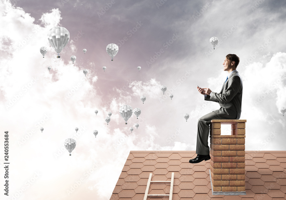 Man on brick roof using smartphone and aerostats flying in air Man on brick roof using smartphone and aerostats flying in air