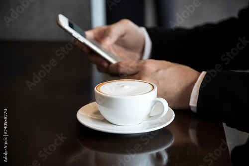 Business man using mobile phone while drinking coffee in coffee shop - modern life style business man in coffee shop concept