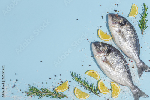 Fototapeta Naklejka Na Ścianę i Meble -  Raw dorada fish with spices, salt, lemon and herbs, rosemary on a ligth-blue background. Top view.