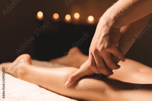 Close-up of male hands doing calf massage of female legs in a dark room with candles in the background. Cosmetology and spa treatments