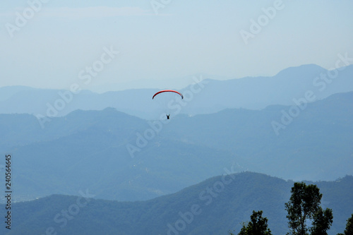 Paragliders are circling in an ascending current above the mountain Sarangkot. Blue sky, multi-colored wings.