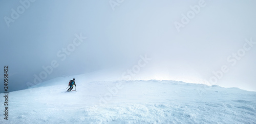 Fast going skier ride down the mountain hill into the storm clouds. Active winter sport concept image.