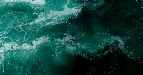 Slow motion top down aerial view of giant ocean waves crashing on sunny day 