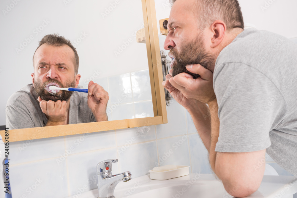 Fototapeta premium Bored guy brushing his teeth in bathroom