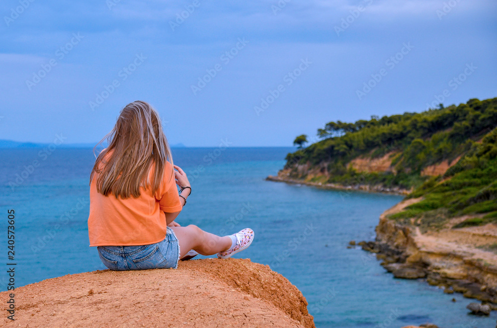 Girl sitting on a cliff above the sea
