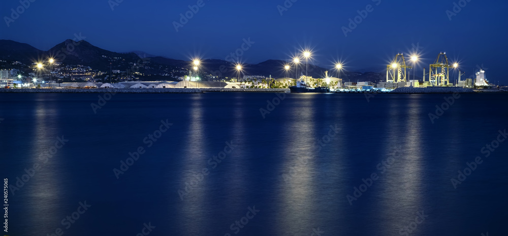 view of Malaga's port, with lights reflecting in the water surface at blue hour, Spain