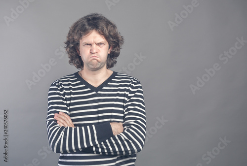 Angry young man in striped sweater puffed up his cheeks and crossed arms about to have nervous breakdown, isolated on gray wall background. Negative human emotions facial expression feelings attitude