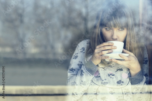 Fotografía winters day, young woman in pijama drinking hot coffee looking out through window on a cold morning