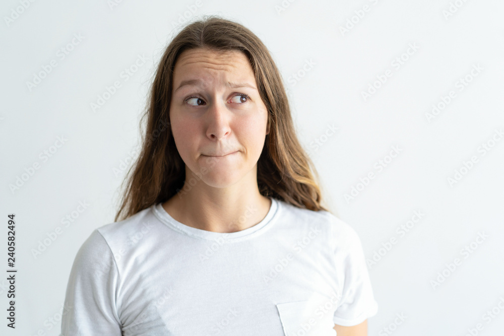 Fototapeta premium Embarrassed young woman pursing mouth. Lady looking away. Bewilderment concept. Isolated front view on white background.