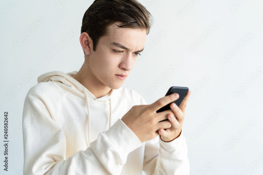 Focused teen boy holding and using smartphone. Technology concept. Isolated front view on white background. Focused teen boy holding and using smartphone. Technology concept. Isolated front view on white background.