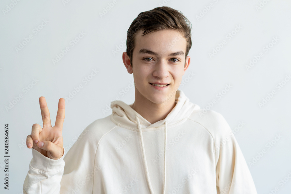 Smiling teen boy showing victory sign and looking at camera. Attractive young guy celebrating success. Victory concept. Isolated front view on white background. Smiling teen boy showing victory sign and looking at camera. Attractive young guy celebrating success. Victory concept. Isolated front view on white background.