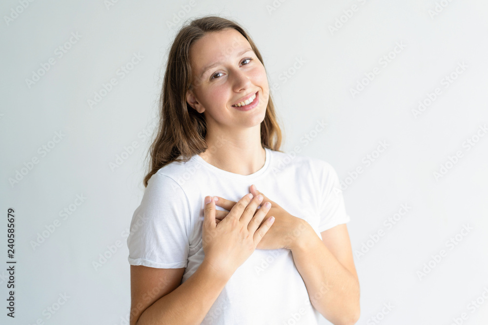 Thankful young woman keeping hands on chest and looking at camera. Pretty girl thanking somebody. Gratitude concept. Isolated front view on white background. Thankful young woman keeping hands on chest and looking at camera. Pretty girl thanking somebody. Gratitude concept. Isolated front view on white background.