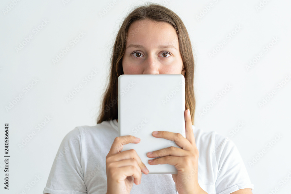 Young woman holding tablet computer in front of face. Pretty lady using digital device and looking at camera. Technology concept. Isolated front view on white background. Young woman holding tablet computer in front of face. Pretty lady using digital device and looking at camera. Technology concept. Isolated front view on white background.