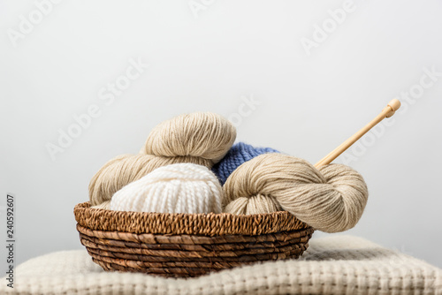 close up view of yarn with knitting needles in wicker basket on grey backdrop