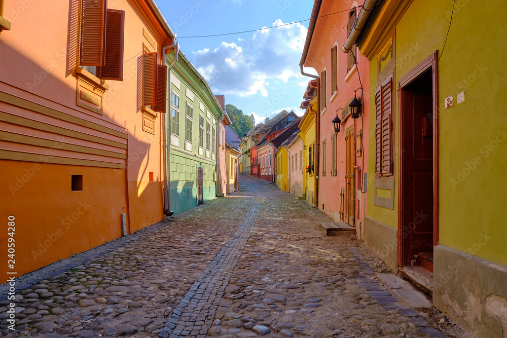   Empty cobbled stone street of 18th century Sighisoara city with colorful houses in the old historical part of town.