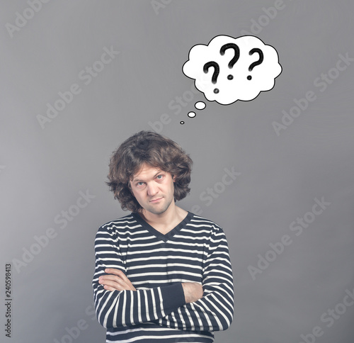 Skeptical man looking suspicious and questionable with drawn cloud of thoughts with three question marks in it. Some disapproval on face on gray background. Human emotions facial expressions feelings