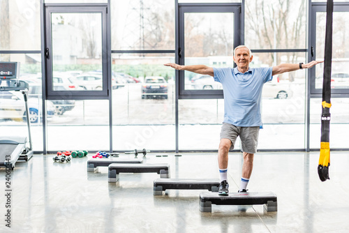 Fototapeta Naklejka Na Ścianę i Meble -  cheerful senior sportsman exercising on step platform at gym