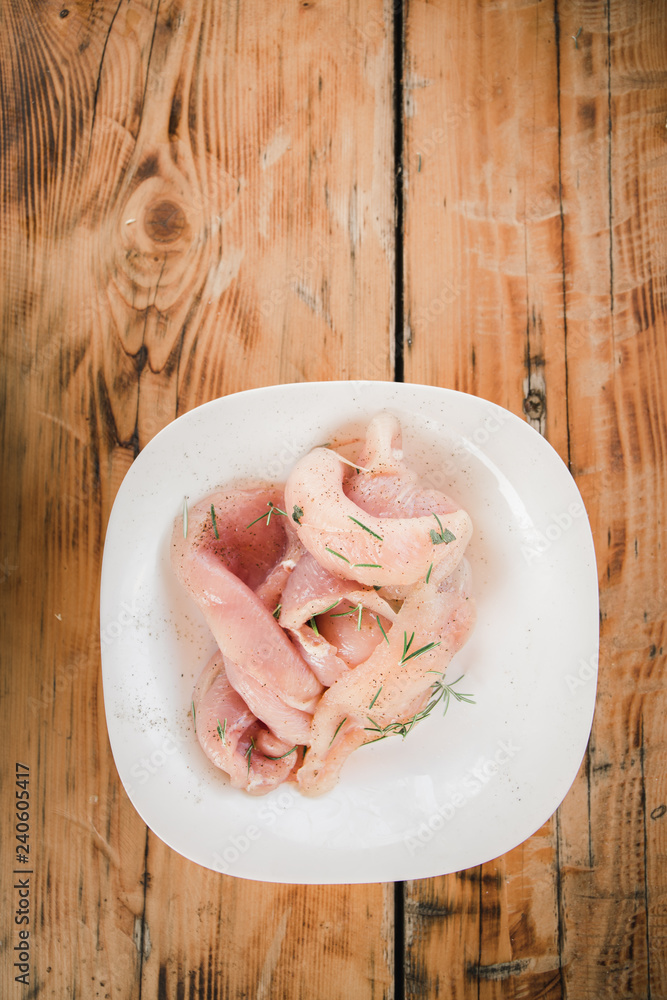 Fresh organic chicken meat on white dish with rosemary on the wooden table Fresh organic chicken meat on white dish with rosemary on the wooden table