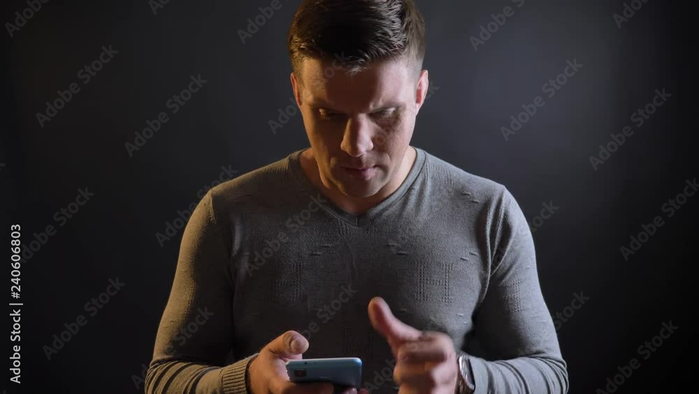 Close-up portrait of middle-aged caucasian man watching attentively into smartphone on black background. Close-up portrait of middle-aged caucasian man watching attentively into smartphone on black background.