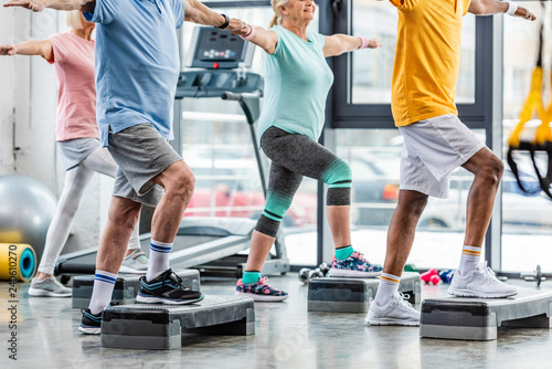 Fototapeta Naklejka Na Ścianę i Meble -  partial view of senior athletes synchronous exercising on step platforms at gym