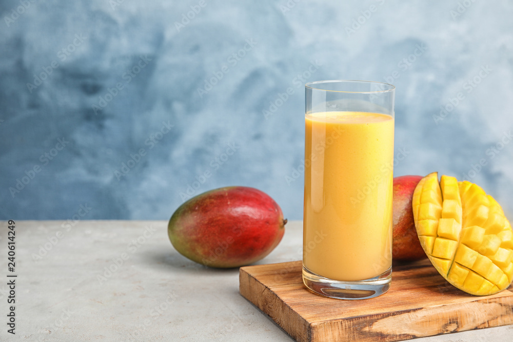 Glass of fresh mango drink and fruits on table against color background. Space for text Glass of fresh mango drink and fruits on table against color background. Space for text